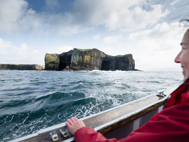 A woman on a boat looking out to a dramatic rocky crag in the sea.
