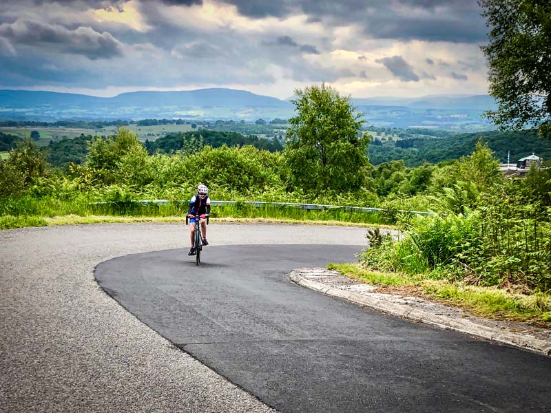 Low carbon travel - a road cyclist coming round a corner in a lush green setting