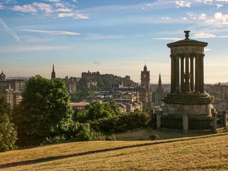 Panoramic view of Edinburgh skyline with historic buildings, the Scott Monument, and Castle in the distance.