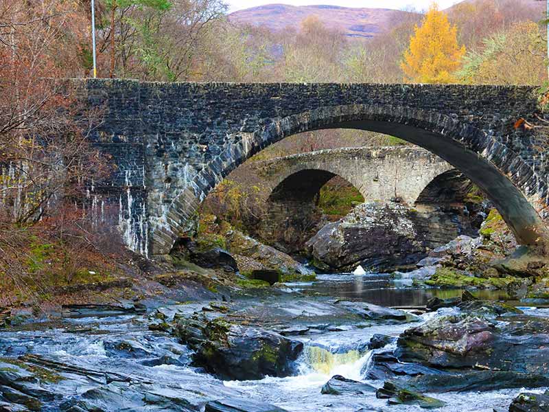 A picture of two bridges over a river, surrounded by autumn colours