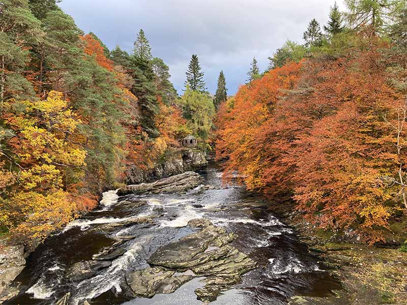 a small hermitage sitting above a river with autumn colours