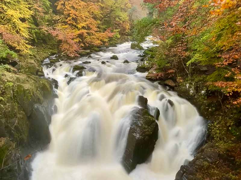 A waterfall in spate surrounded by autumn colours in Perthsire