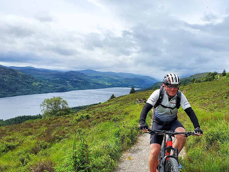 Low carbon travel - man biking towards the camera with the Scottish Highlands as a backdrop. 