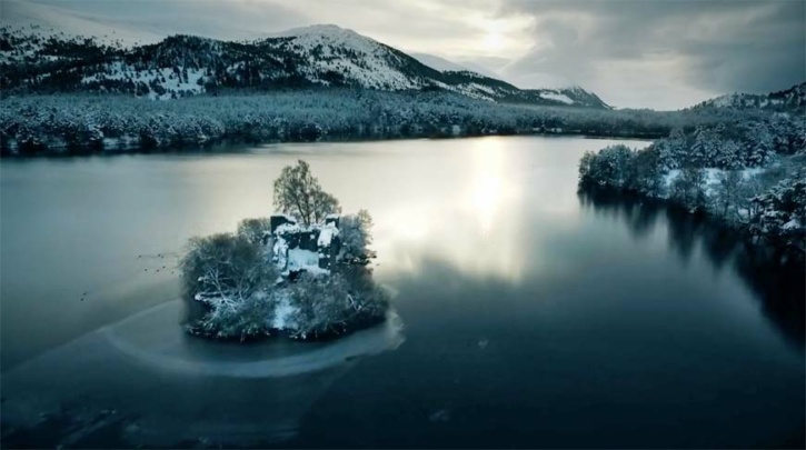 Loch an Eilein Castle from the air in winter with ice on the loch and snow on Creag Dubh in the background.