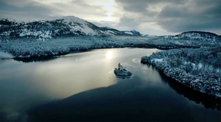An ariel image of Loch an Eilein during winter. You see the 13th Century island castle with snow in the ancient pine trees and Creag Dubh behind.