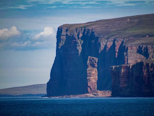 Dramatic cliffs plunge into the ocean with aa seastack in front.