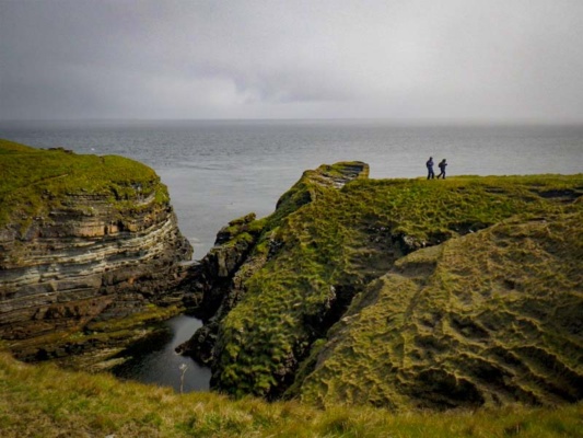 Olive green grass tops striated grey cliffs under moody skies over swirling seas.