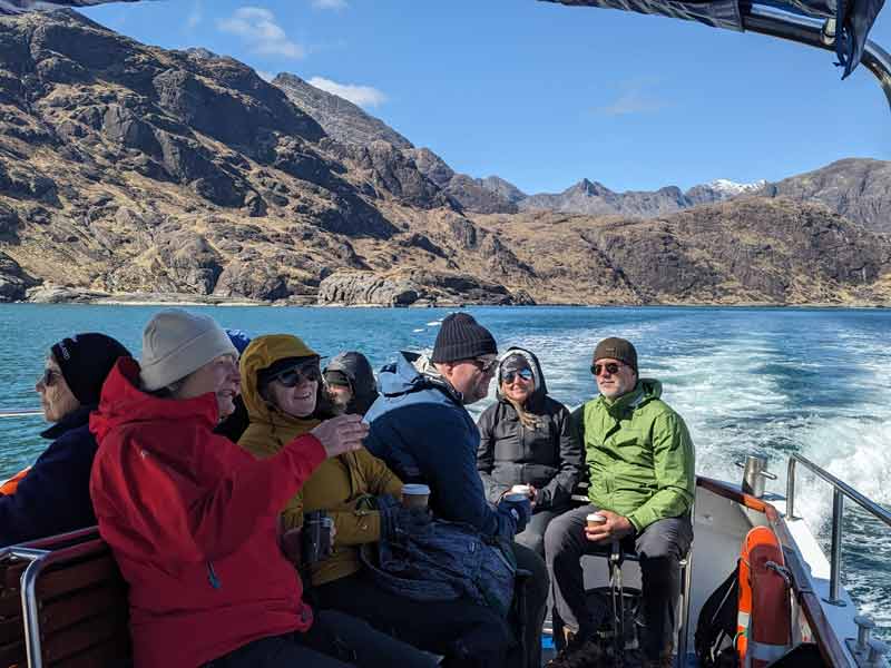 people on a boat with dramatic scenery and very blue water in the background. The people are dressed warmly.