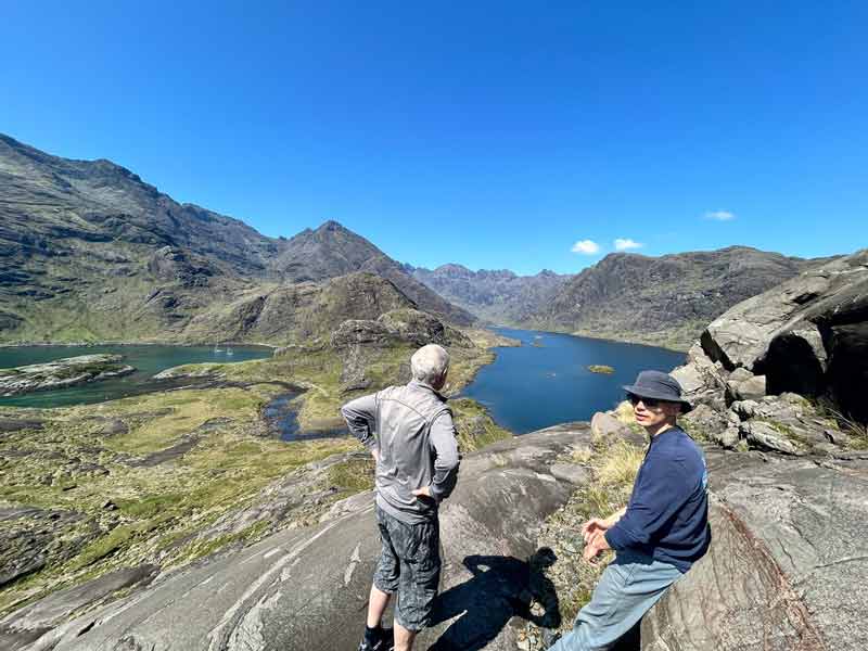 two people overlooking dramatically set mountain loch, rocky terrain with tall mountains